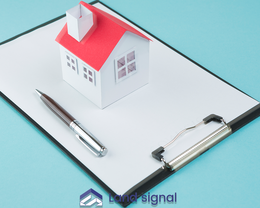 Mini house model and pen resting on blank clipboard against blue background.”